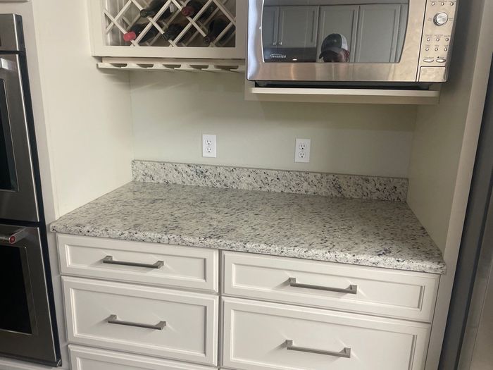 A kitchen with white cabinets , granite counter tops , stainless steel appliances and a wine rack.