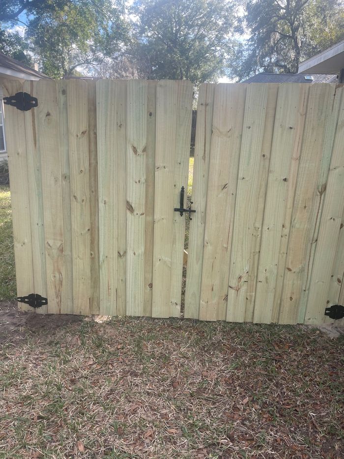 A wooden fence with a gate is sitting on top of a lush green field.