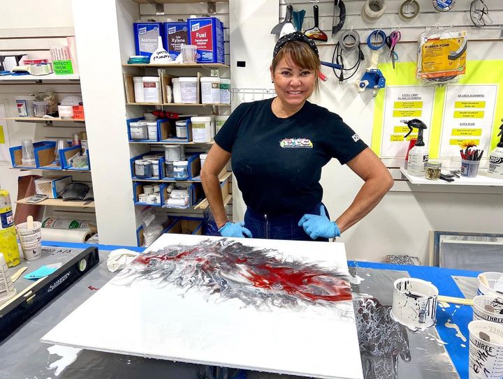 A woman is standing in front of a painting on a table.
