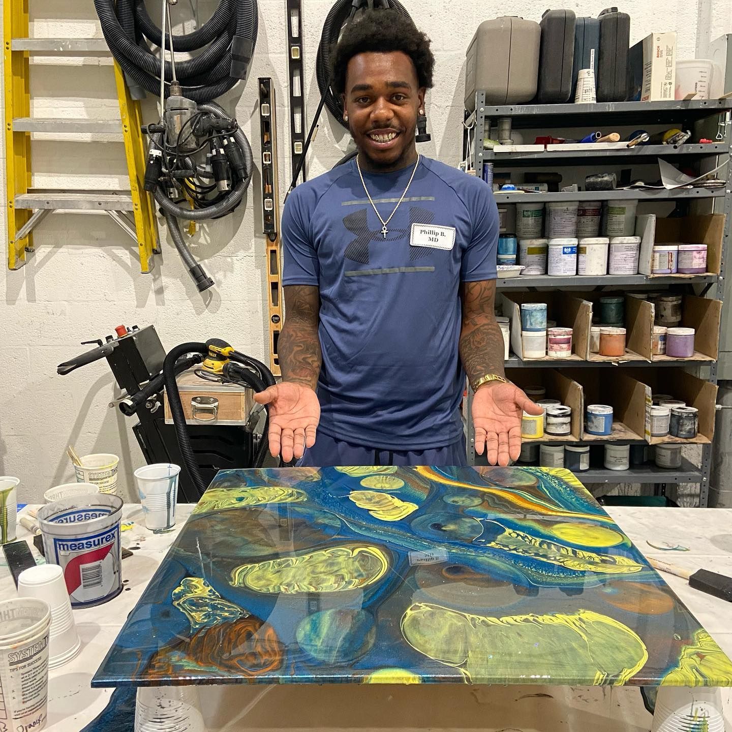 Smiling person in a workshop, presenting a colorful abstract painting on a table.