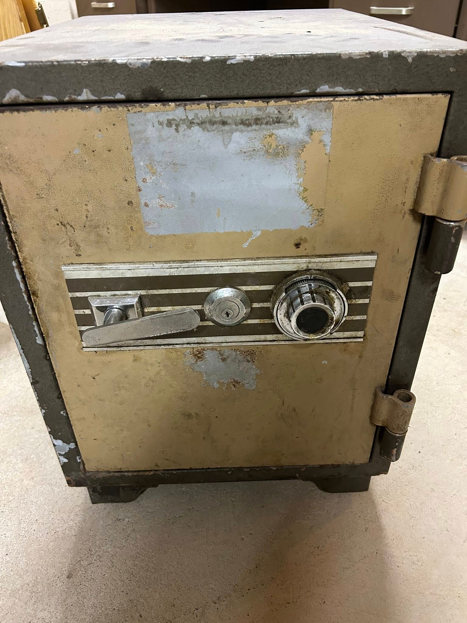 A weathered, tan and gray safe with a combination dial and lock.