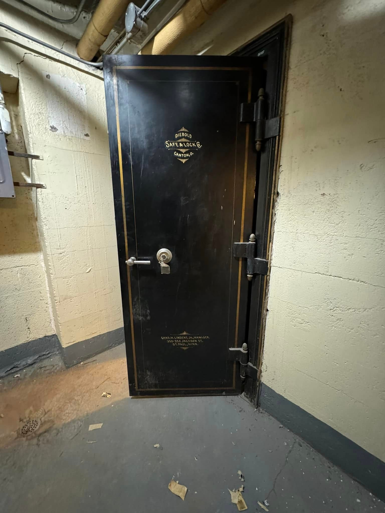 Black vault door with ornate gold trim in a concrete basement.