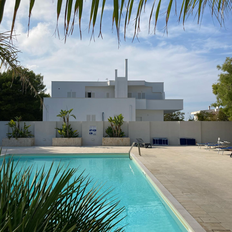 Casa moderna bianca con piscina turchese e patio sotto un cielo azzurro.