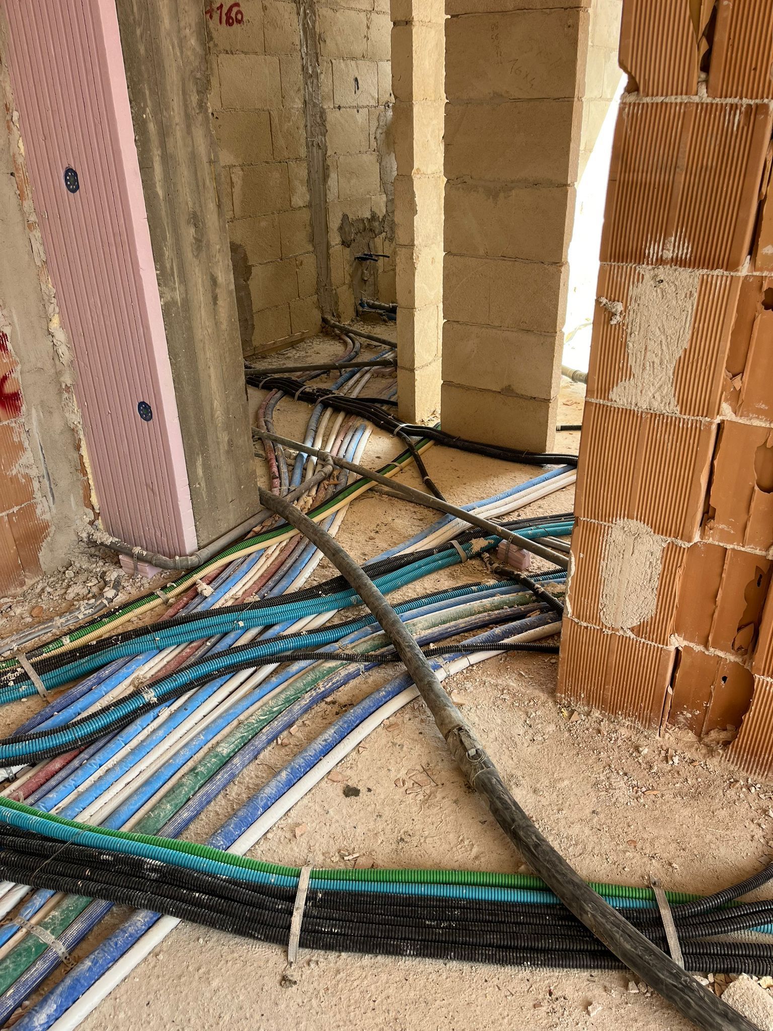 Cantiere edile con muro a vista, cavi a pavimento e un tubo nero che ostruisce l'apertura di una porta.