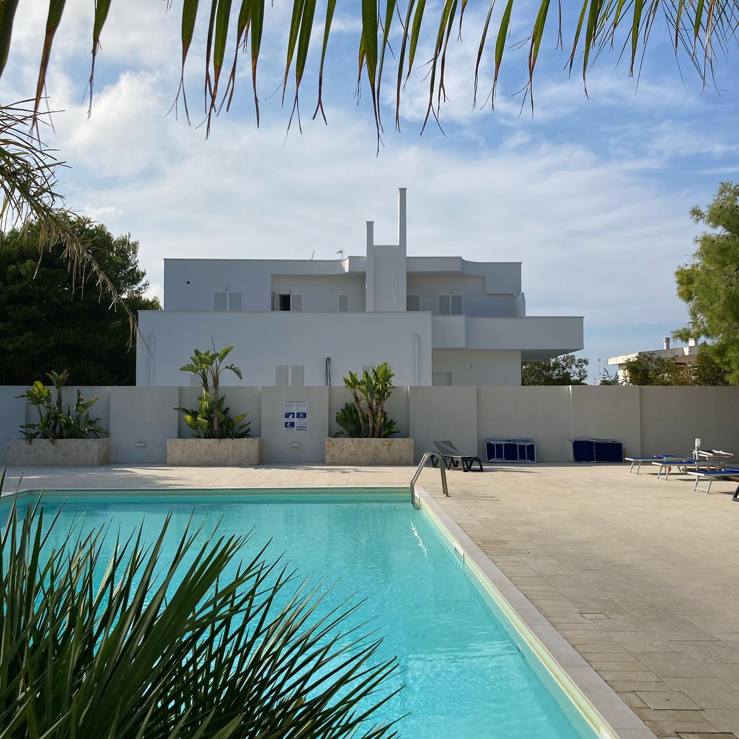 Casa moderna bianca alle spalle di una piscina turchese sotto un cielo azzurro limpido.