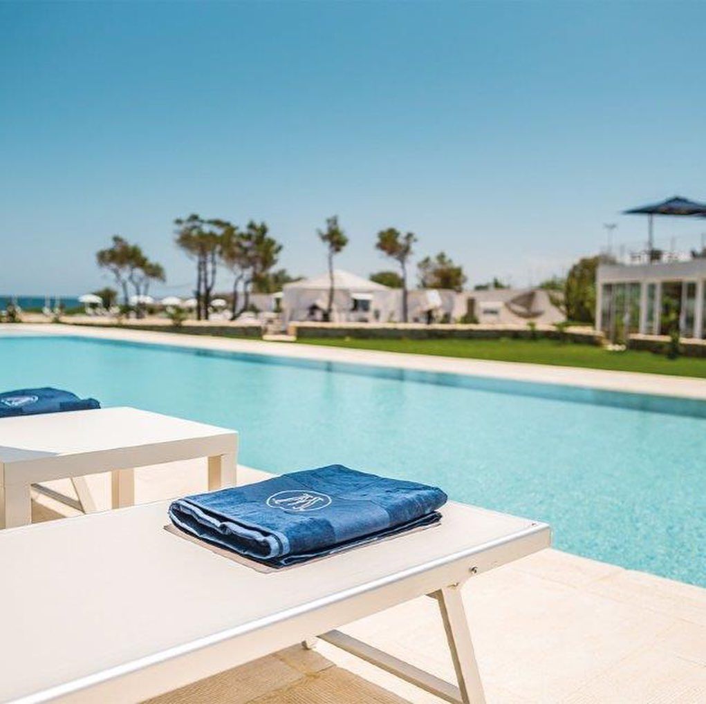 Sedie a sdraio a bordo piscina, accanto a una piscina turchese del resort, sotto un cielo azzurro limpido.
