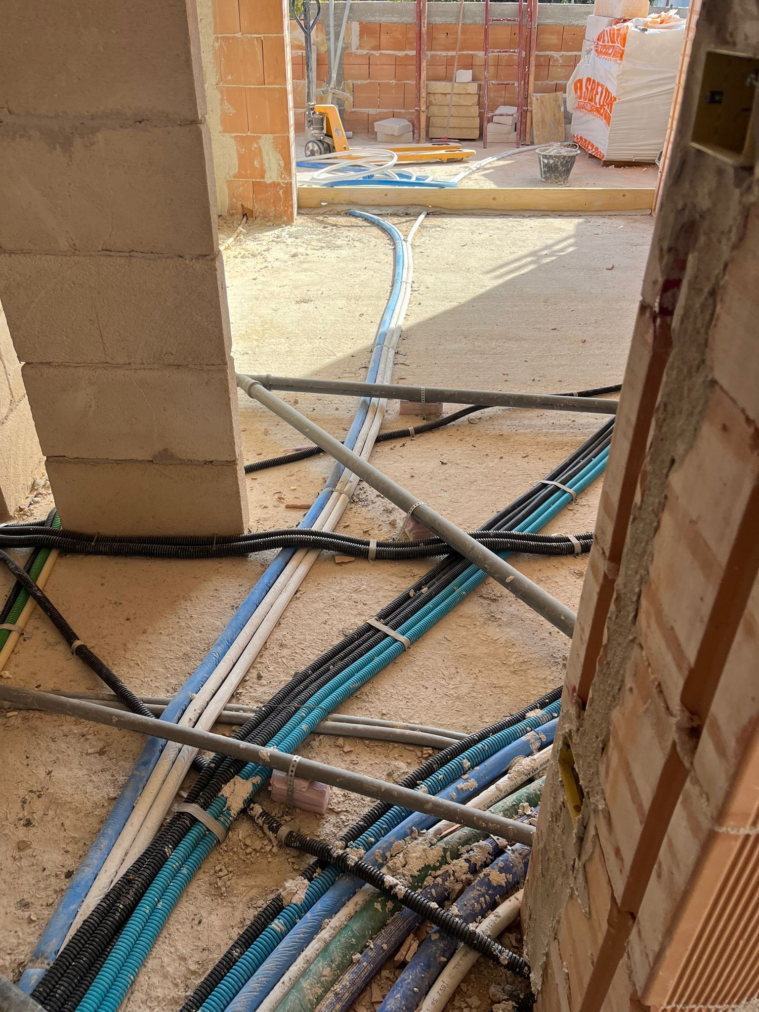 Interno di un edificio incompiuto con mattoni a vista e cavi elettrici aggrovigliati sul pavimento e sulla porta.