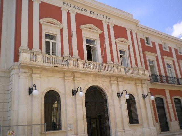Edificio storico del municipio, di colore rosso e bianco, con ingressi ad arco e balconi.