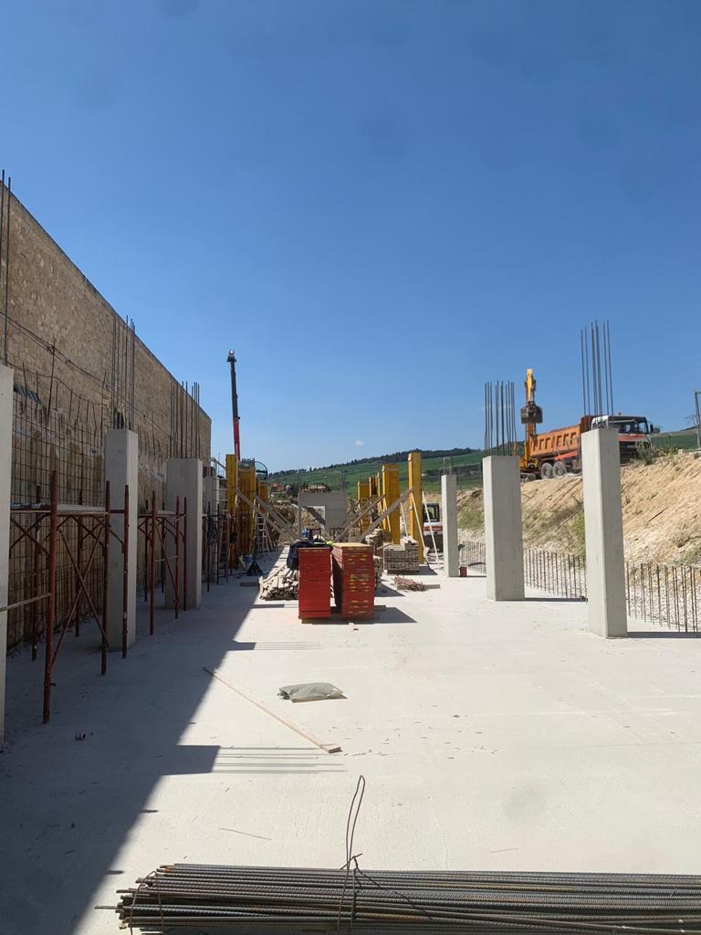 Passeggiata all'aperto con pavimentazione bianca, muri in pietra e materiali da costruzione sotto un cielo azzurro limpido.