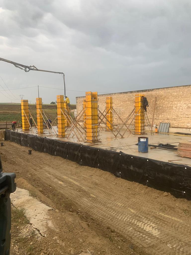 Cantiere edile con pilastri in cemento, impalcature e una gru sotto un cielo nuvoloso.