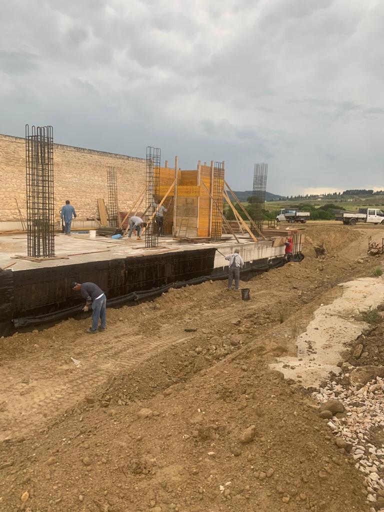 Cantiere edile con operai intenti a gettare le fondamenta in cemento sotto un cielo nuvoloso.