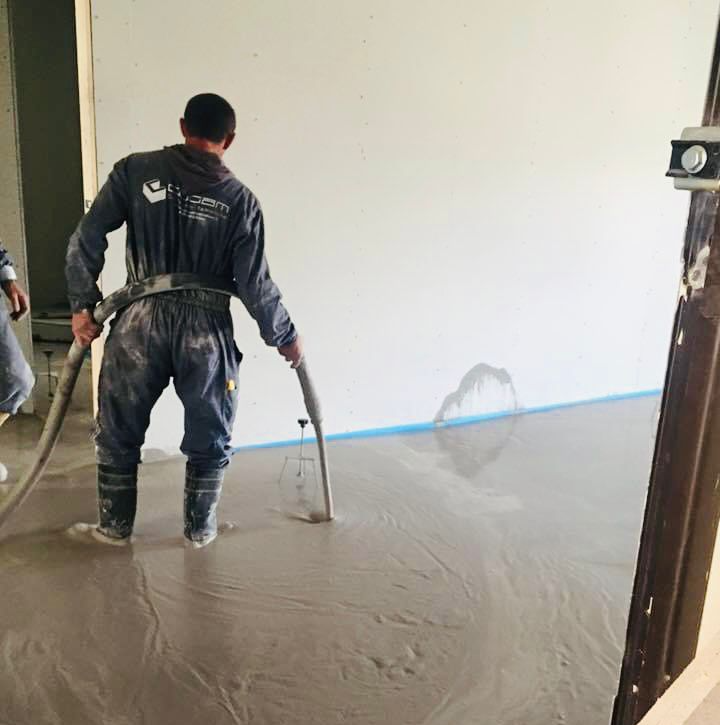 Un operaio liscia un pavimento di cemento fresco all'interno di una stanza, utilizzando un attrezzo a manico lungo.