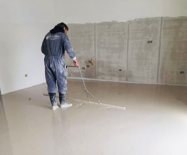 Un operaio con una tuta blu usa un rullo per pavimenti su un pavimento bianco lucido di una stanza.