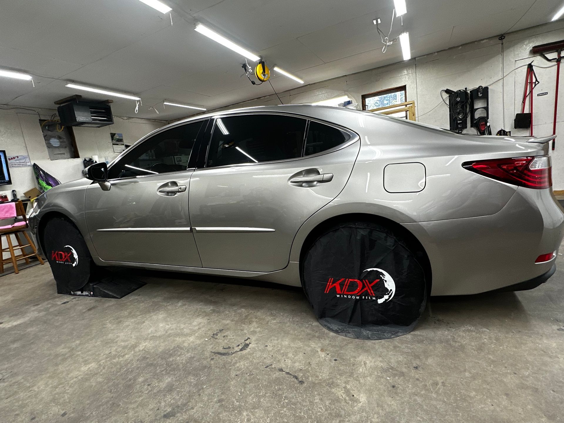 A silver car is parked in a garage with a tire cover on it.