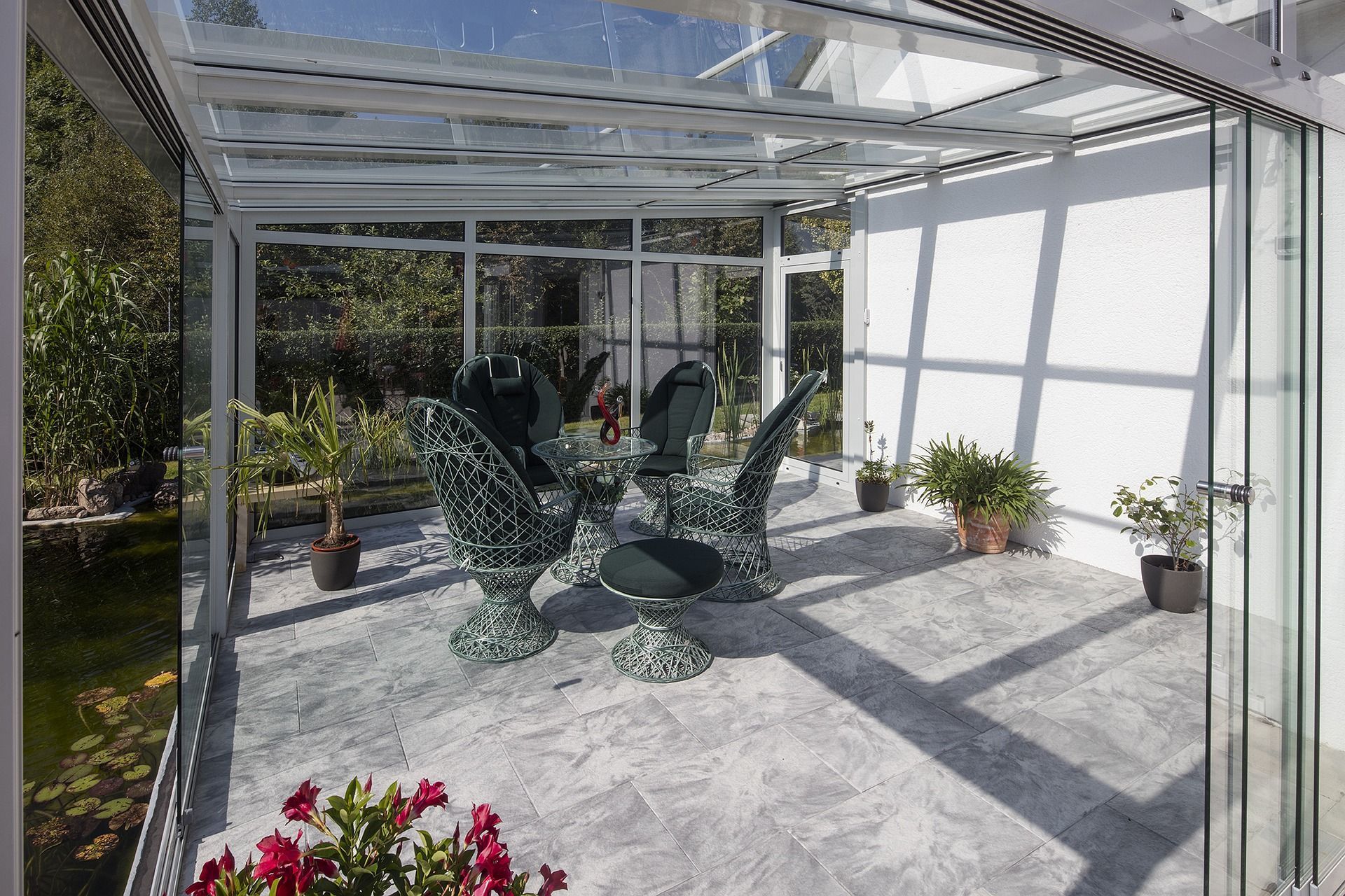 Véranda vitrée avec table et chaises. Des plantes en pot sont disséminées un peu partout