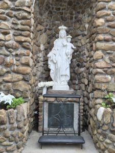 White statue in a stone grotto niche above a fireplace with a black bench in front