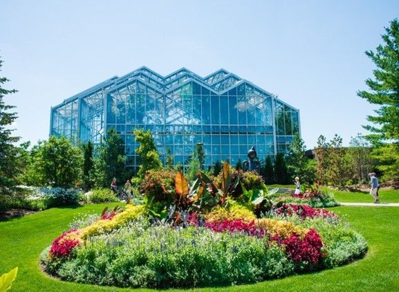 Glass greenhouse behind a colorful flower garden and manicured lawn on a sunny day