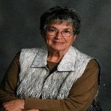 Smiling woman with glasses in a brown top and light gray vest against a dark background