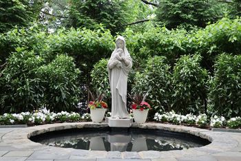 White statue in a garden fountain, surrounded by greenery and flowers