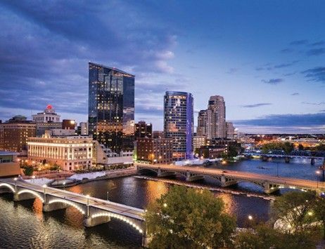 City skyline at dusk with a lit bridge over a river and modern downtown buildings.