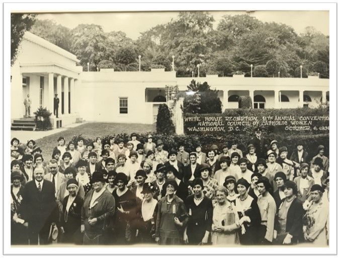 Large group posing in front of a white building and trees, with a statue at the center.