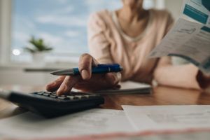 Person using a calculator and holding paperwork at a desk with bills and a pen