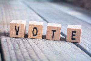 Wooden letter blocks spelling “VOTE” on a gray wooden surface