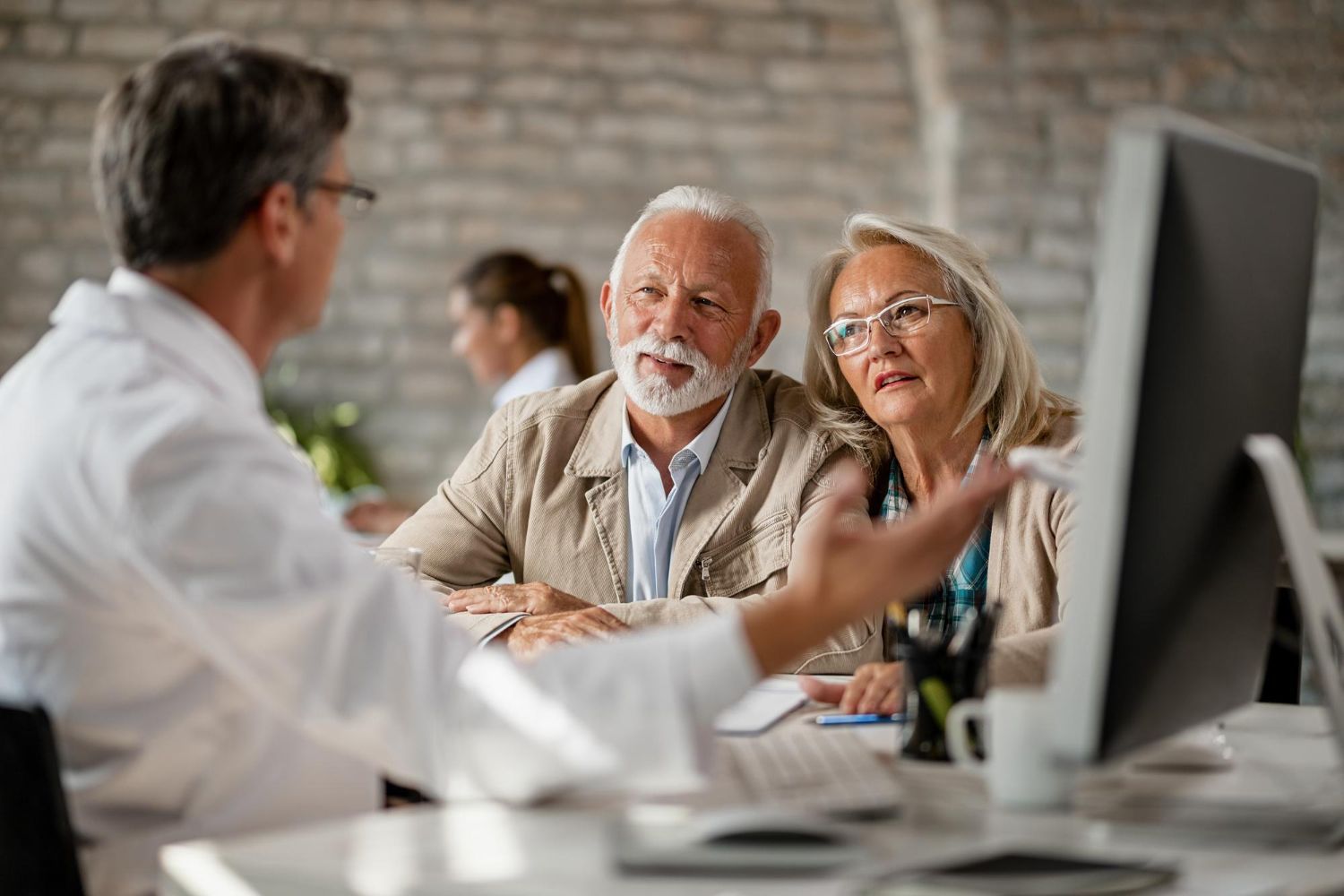 Doctor explaining something on computer to an older couple in a clinic.