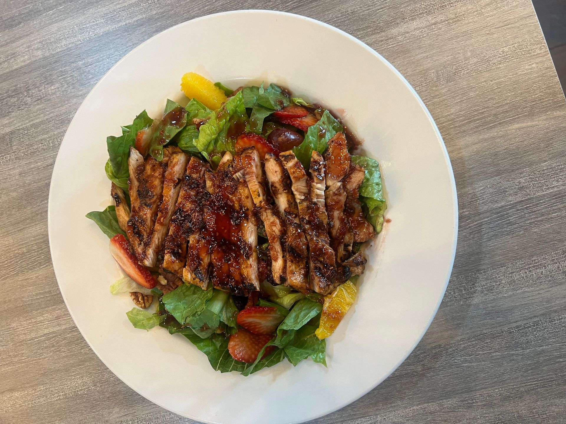 A white plate topped with a salad of meat and vegetables on a table.