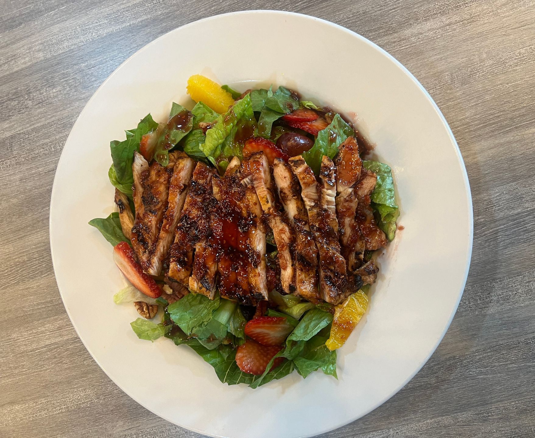 A white plate topped with a salad with meat and vegetables on a table.