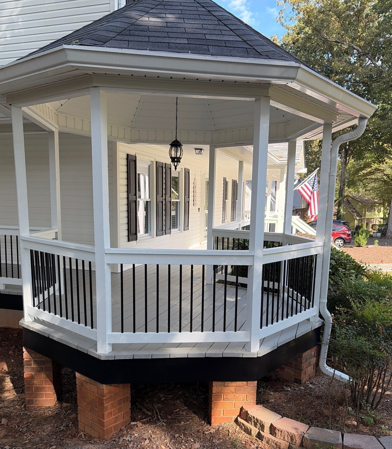 White octagonal gazebo with railing and brick supports in a leafy yard