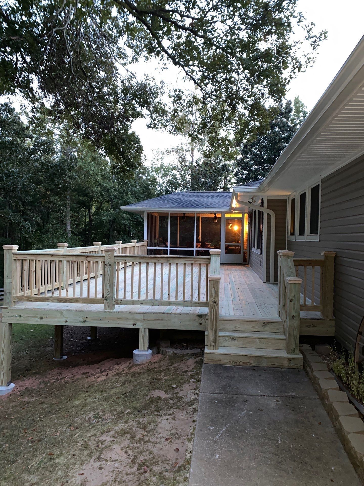 House ramp and porch with wooden deck, steps, and lit entryway under trees