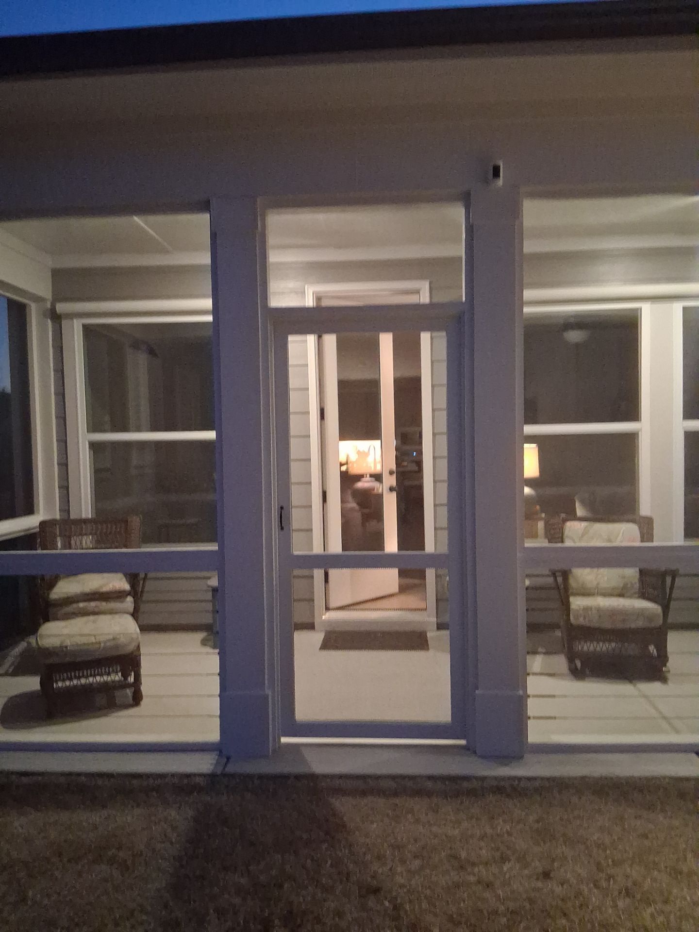 Front porch with a blue front door, white trim, and two cushioned chairs on either side at dusk.