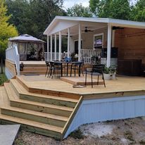 A mobile home with a large wooden deck and stairs leading up to it.