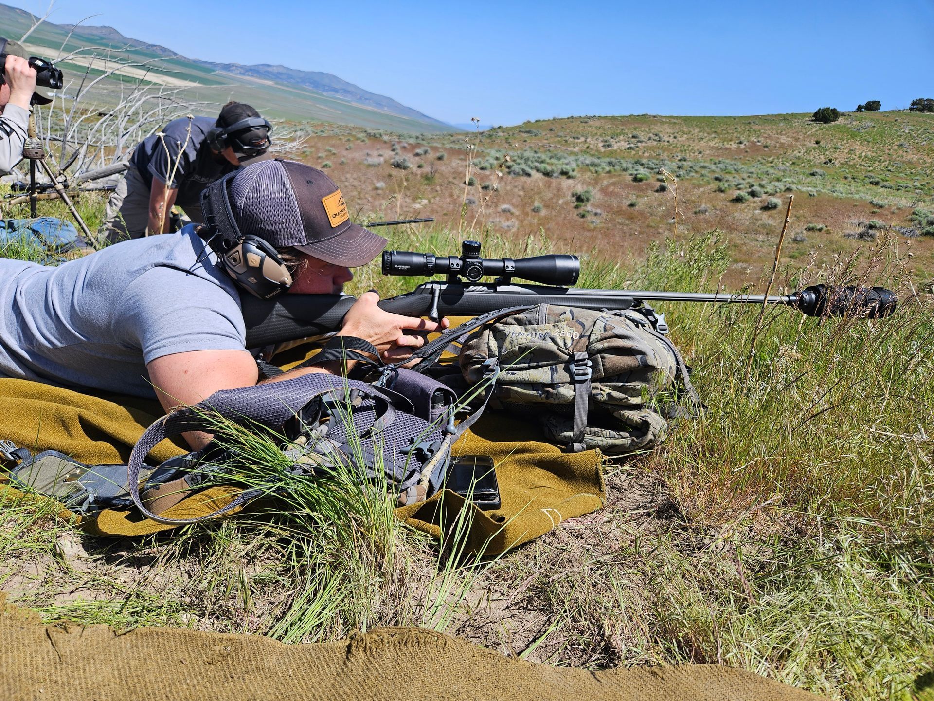 lying shooting a rifle on a mountain with a hat on.