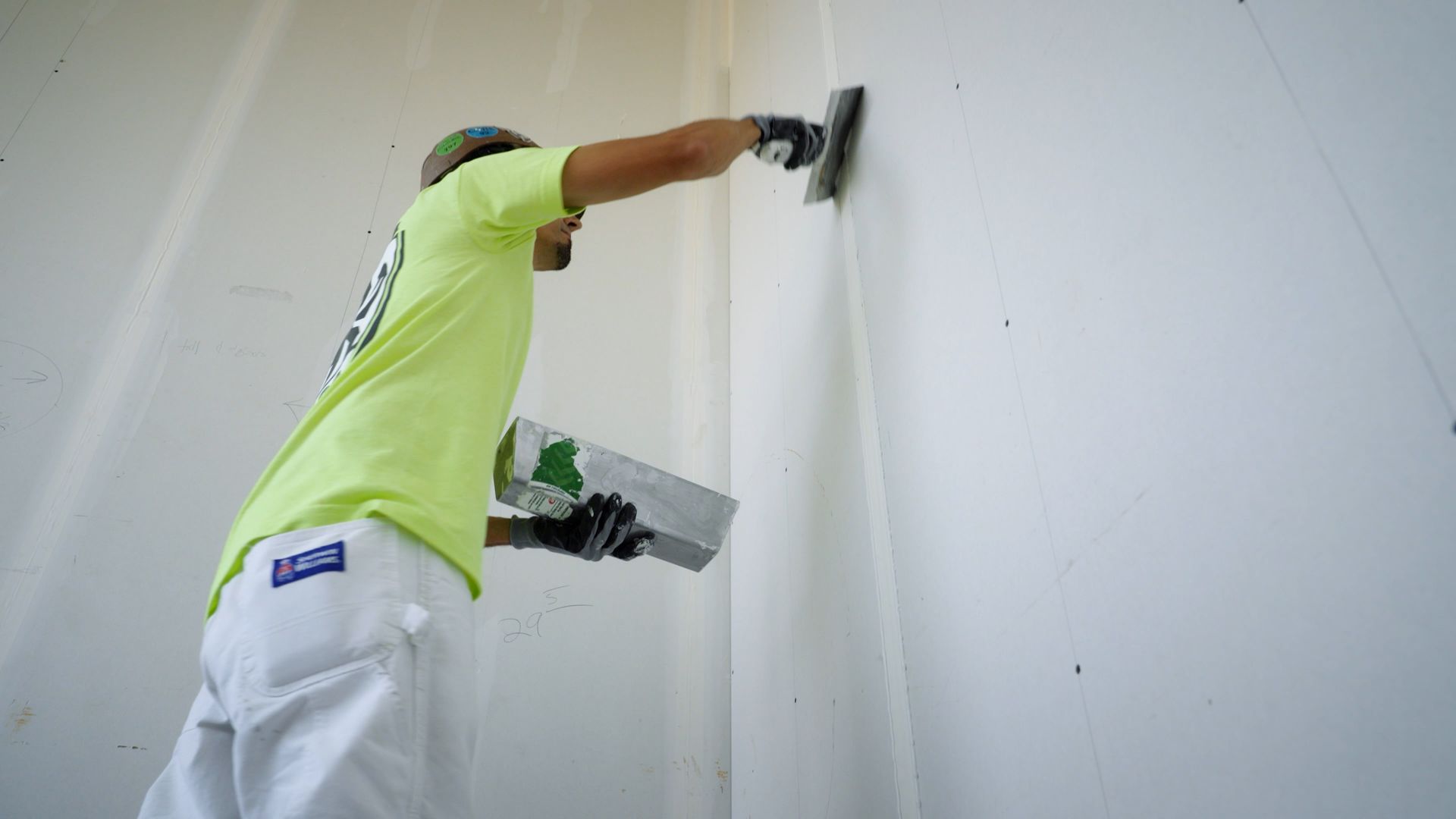 An NCIFTI apprentice using a professional drywall knife to finish a high wall with precision.