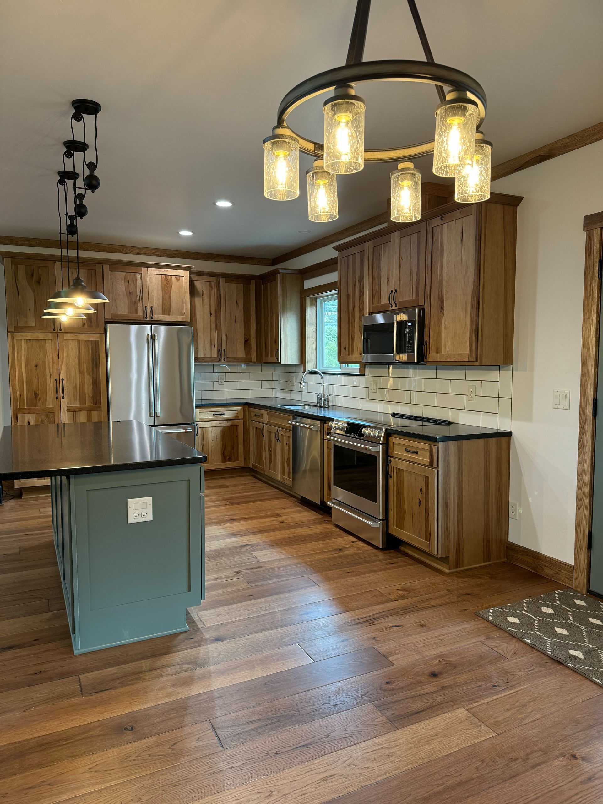 Modern kitchen with wood cabinets, stainless steel fridge, island, and pendant lights over hardwood floors