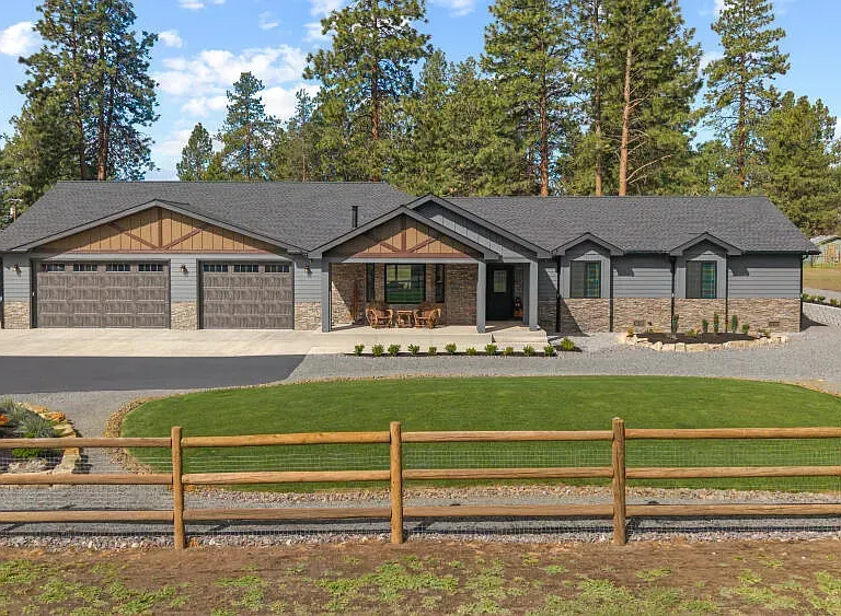 Modern single-story house with stone accents, a three-car garage, and a wooden fence in front of tall pine trees
