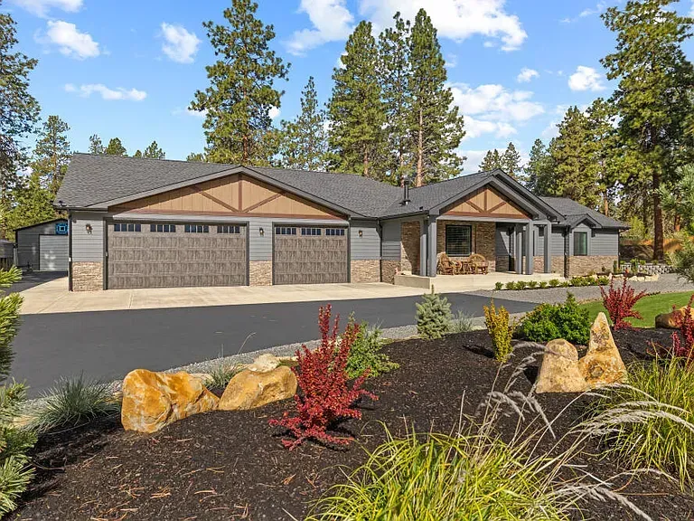 Modern single-story suburban house with three garage doors, stone accents, and landscaped front yard