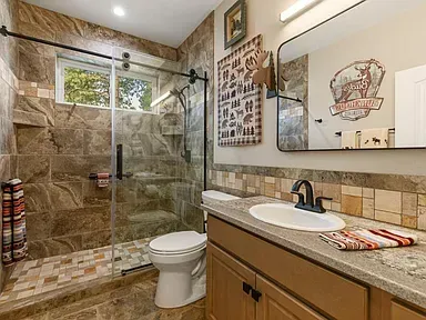 Bright bathroom with tiled shower, vanity, toilet, and large mirror under a sloped ceiling