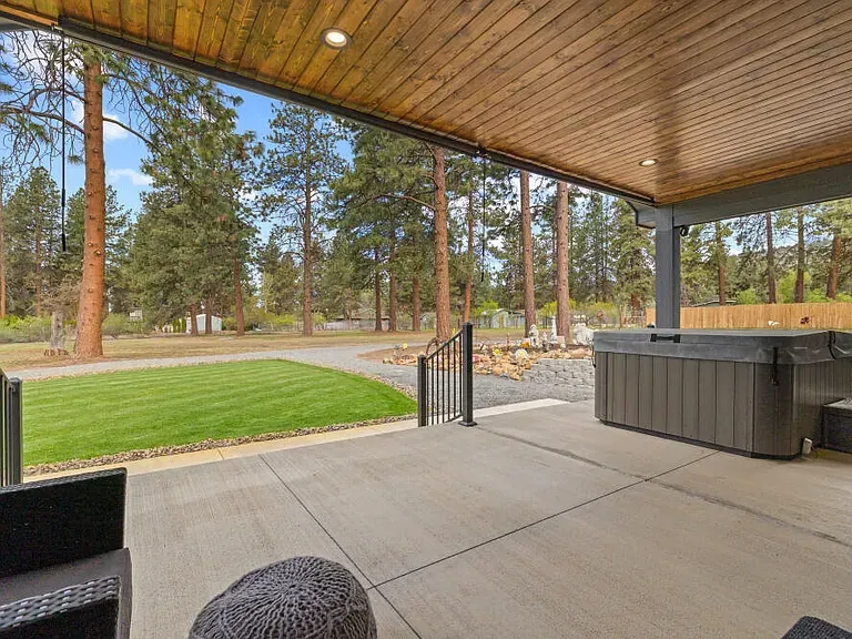 Covered patio with hot tub overlooking a lawn and pine trees