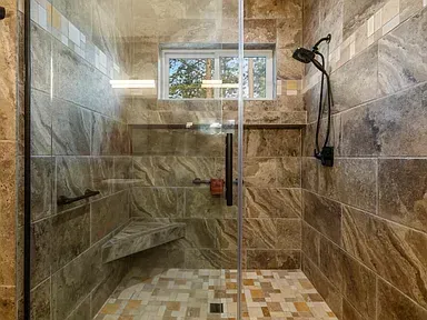 Modern tiled walk-in shower with glass door, bench, window, and rainfall showerhead