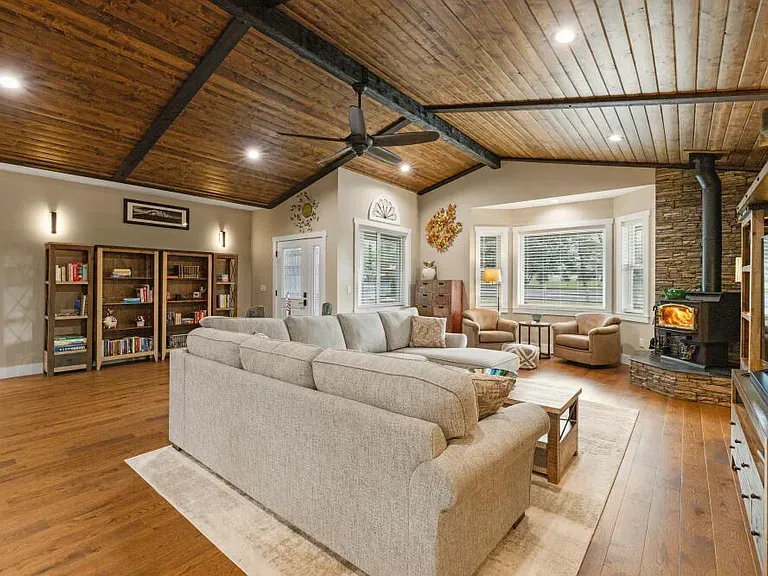 Spacious living room with wood ceiling, beige sofas, fireplace, and large windows with blinds