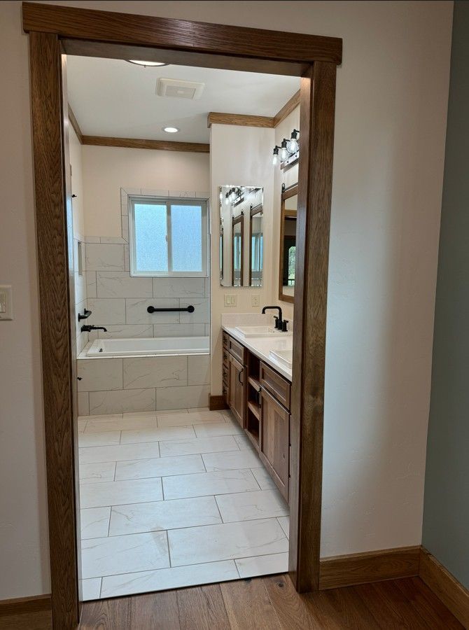 Bathroom doorway with white tile floor, vanity, mirror, and a bathtub in the background