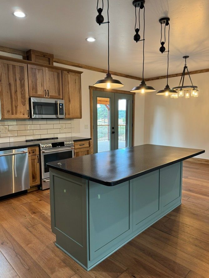 Modern kitchen with a teal island, dark countertop, wood cabinets, stainless appliances, and pendant lights