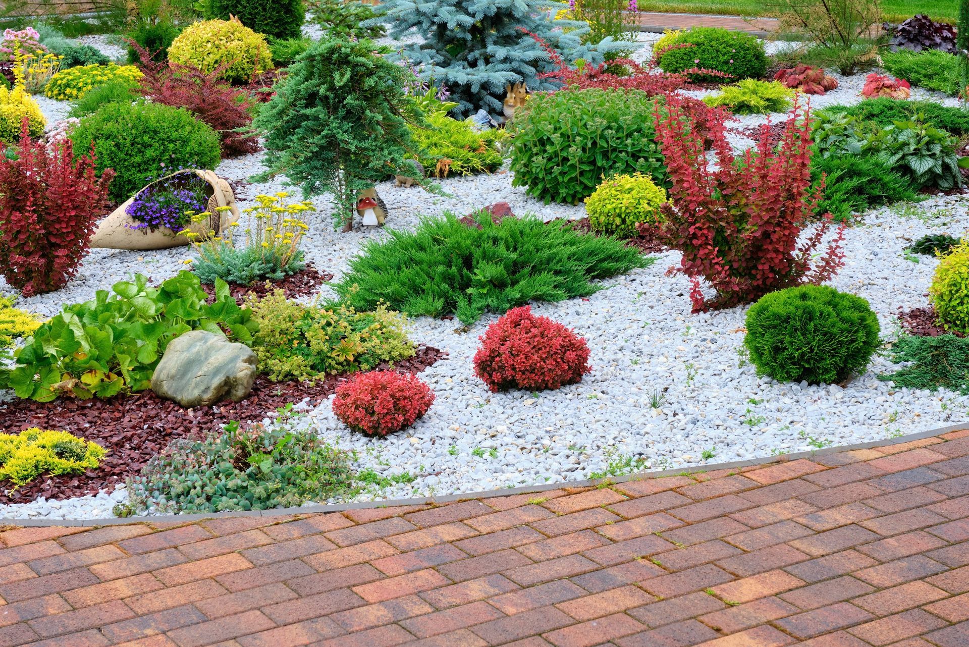 Garden bed with various colorful shrubs and white pebbles.