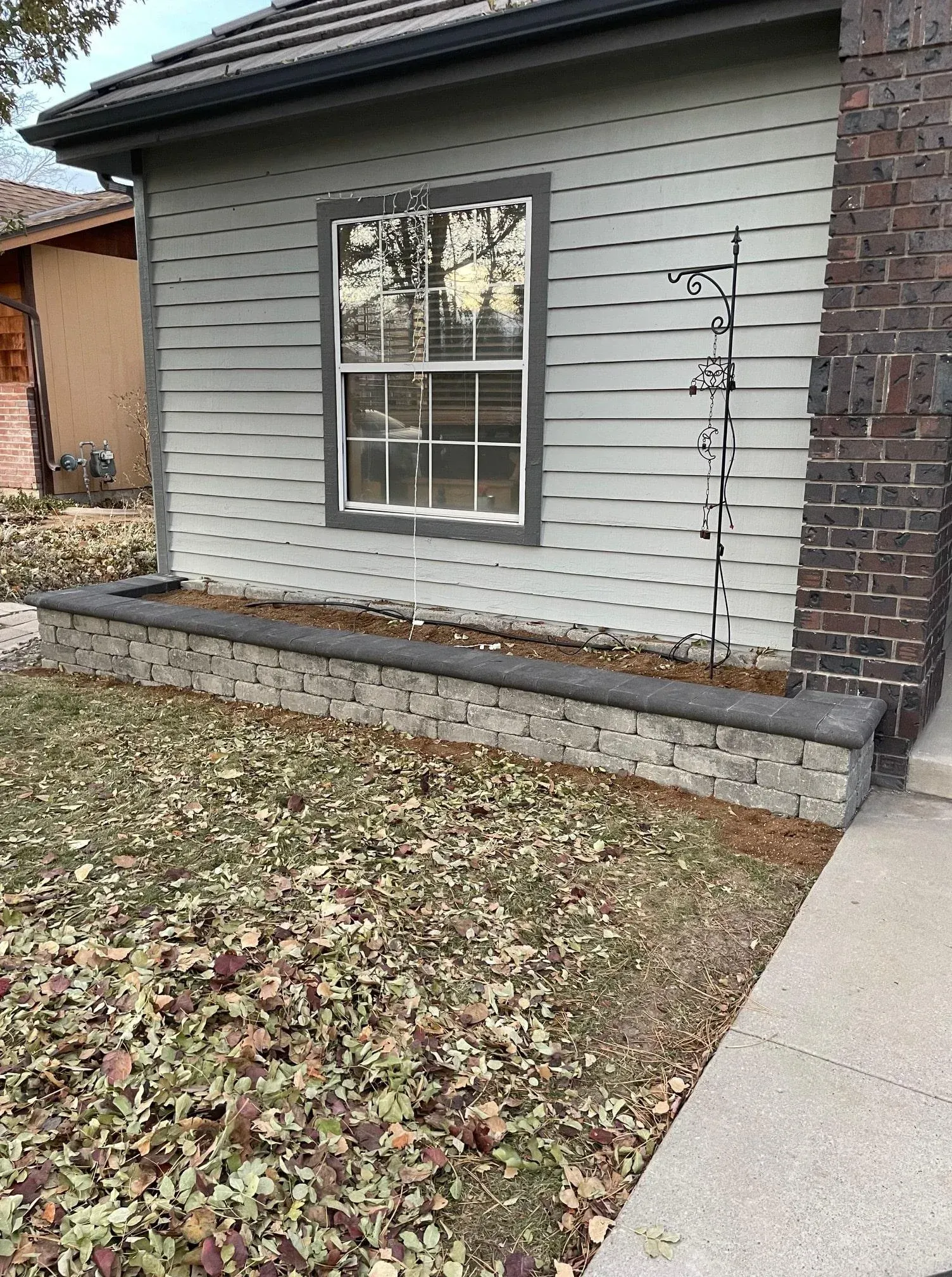 A house with a window, brick chimney, and stone planter box. The yard is covered in leaves.