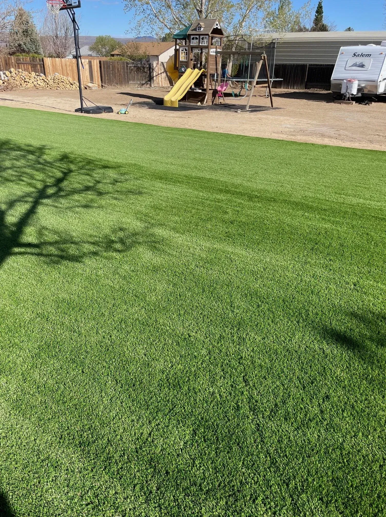 Green artificial turf yard with playground in the background under a sunny sky.