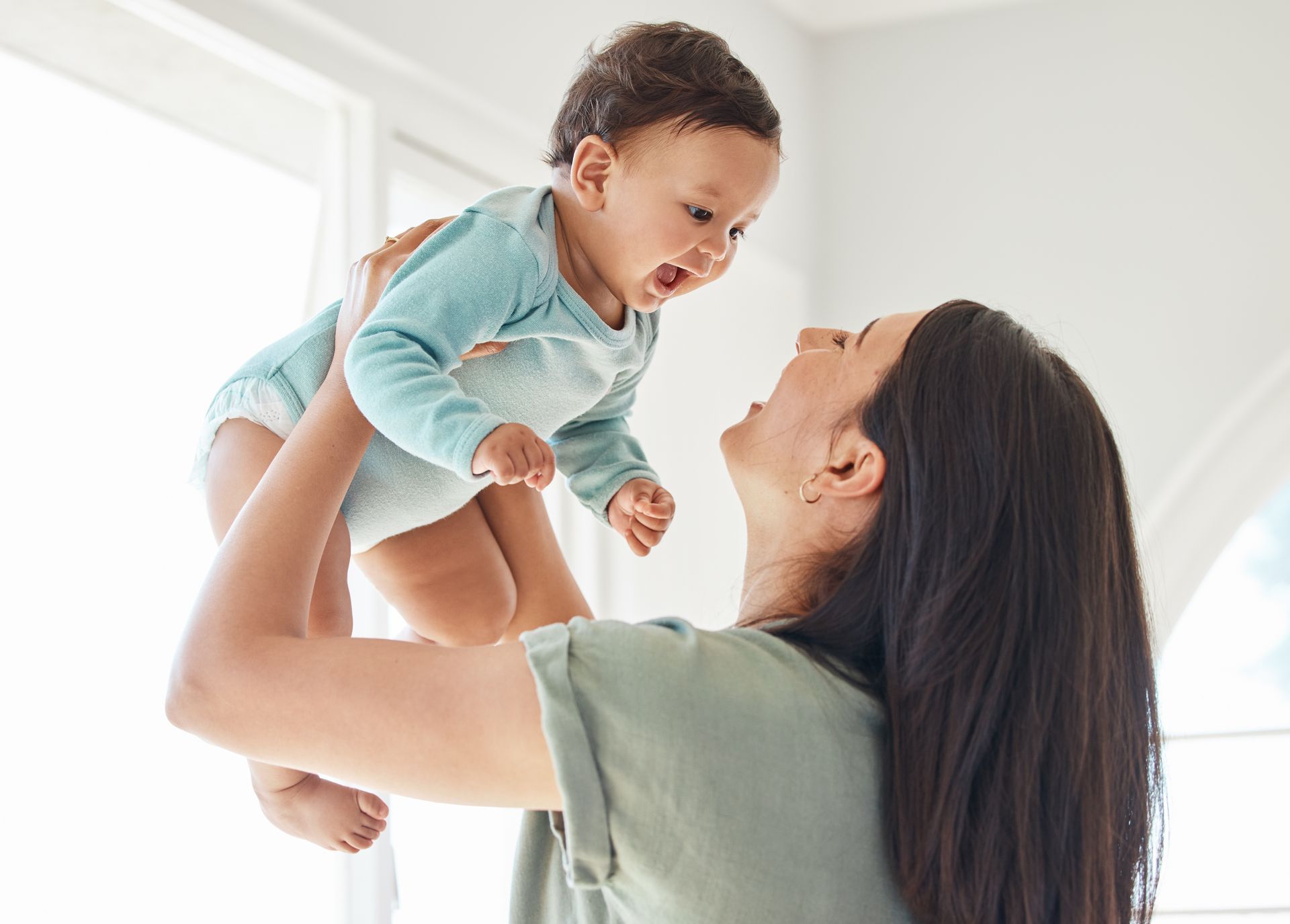 Mother lifting her laughing baby in the air in a bright room