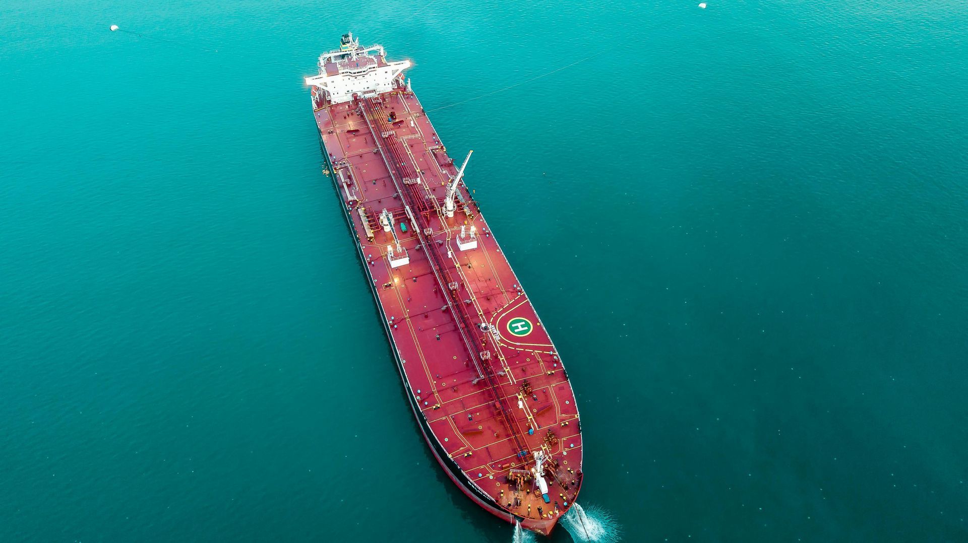 Aerial view of a large red oil tanker ship floating on blue water.
